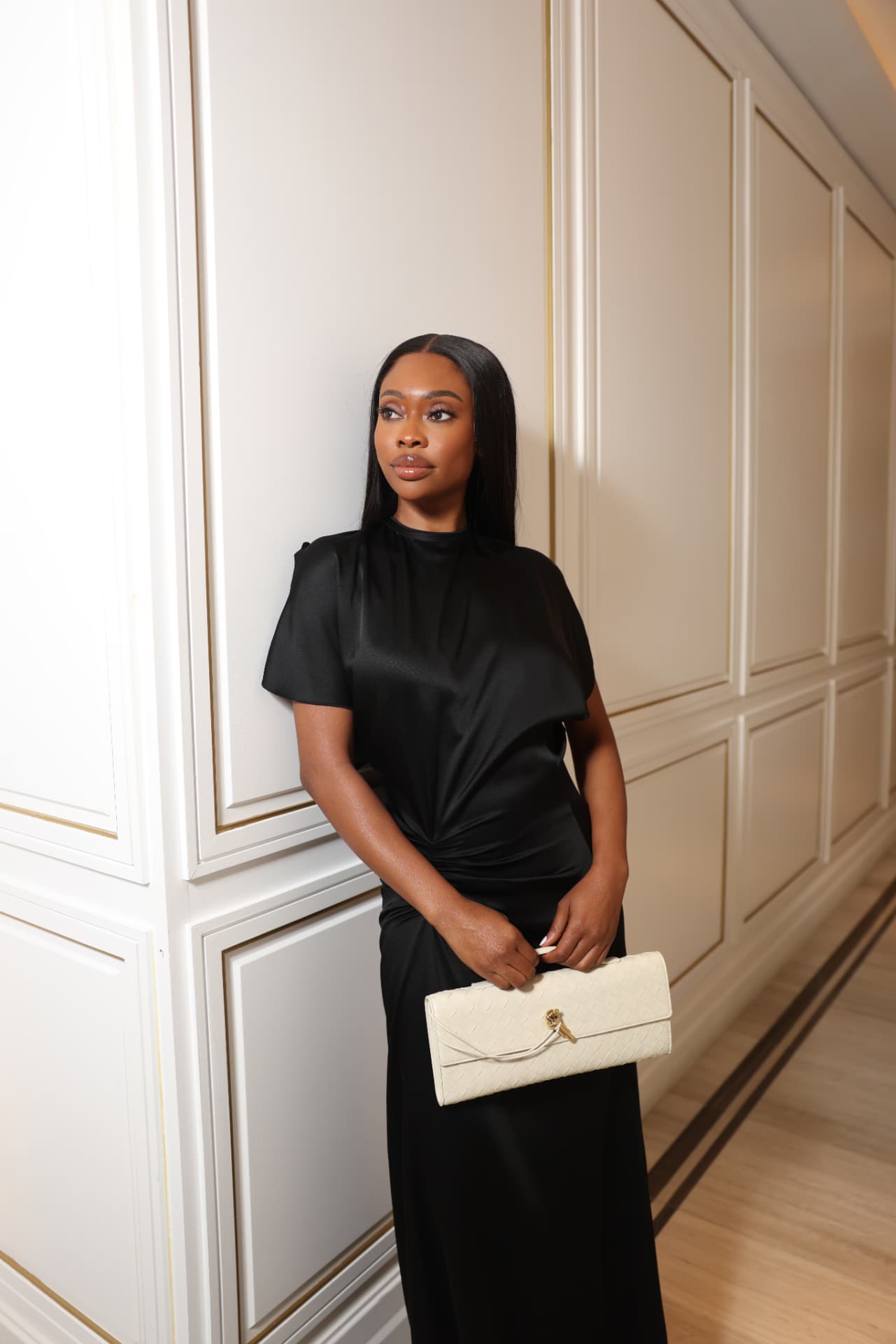 Lateefat Ayinde, founder of Stile.ng, in a black satin gown holding a cream woven clutch